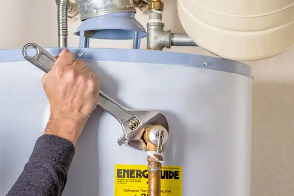 A person skillfully uses a wrench to tighten a valve on a water heater, with the yellow energy guide label prominently visible, expertly handling the water heater repair.